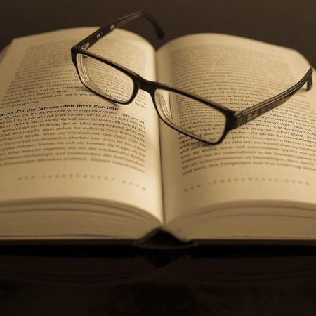A picture of glasses resting on an open page of a text based book.