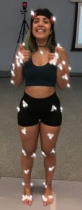 An image of a young woman, wearing black sports clothes. She has lights taped allover her body with white tape.