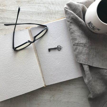 Image of a book, key and glasses resting on a table.